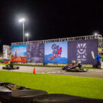 Go-karts race on the main straight at K1 Circuit with a promotional backdrop set up along the straight